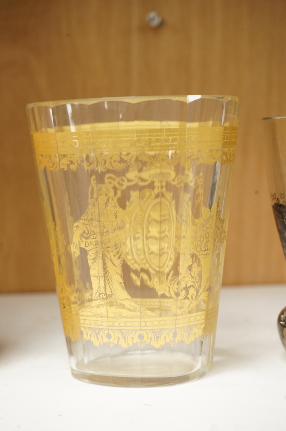 An Italian gilt-decorated and faceted beaker, inscribed Daniel Delvinis, the reverse with papal coat of arms, and a German Schwarzlot black enamelled ‘hunting’ beaker, largest 12cm (2)